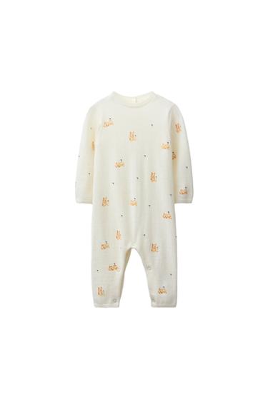 Front view of a long white playsuit with a teddy bear print, round neck and long sleeves. Button fastening at the back.