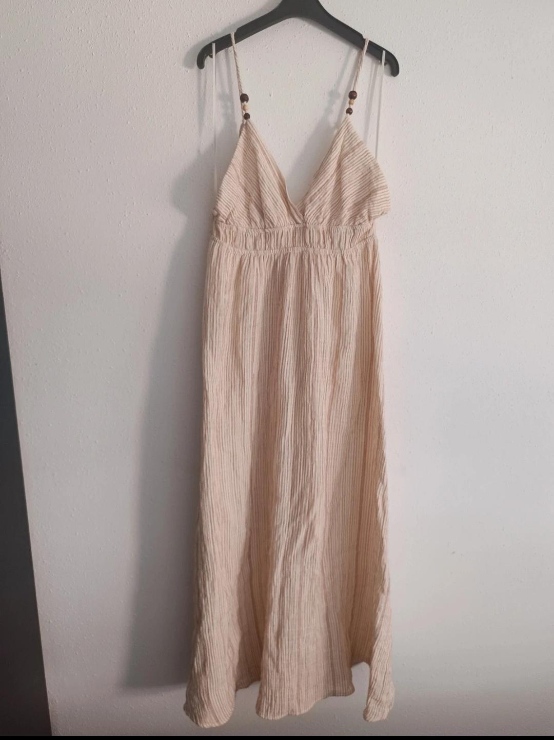 Beige long dress with thin straps and a V-neck, hanging on a black hanger against a white wall.