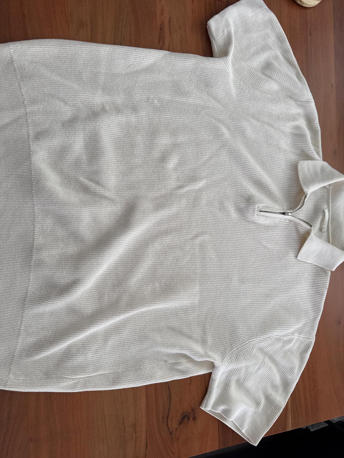 White short-sleeved polo shirt, with a ribbed texture, laid flat on a wooden table.