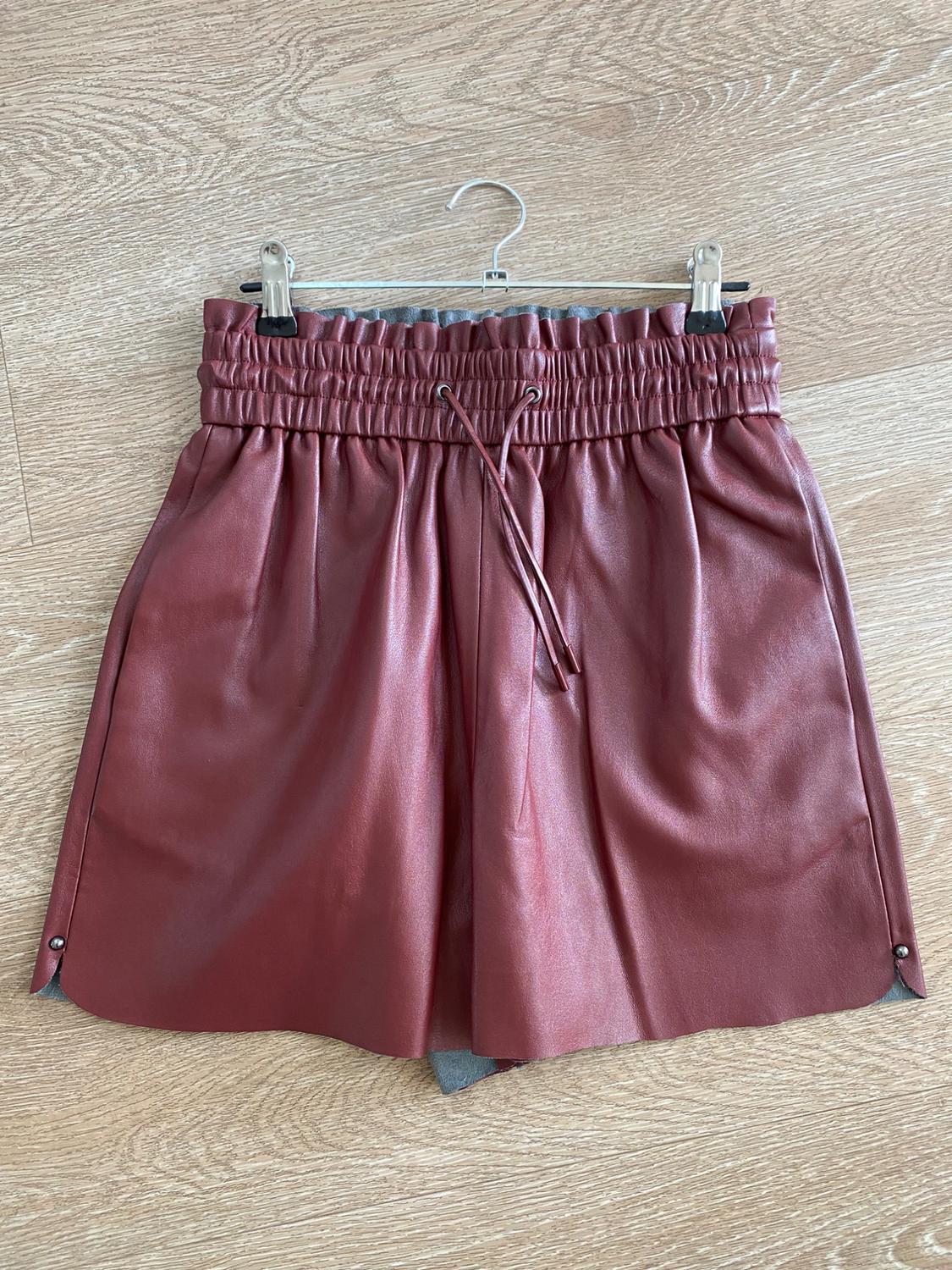 Rust-colored shorts with an elastic waistband and drawstring, hanging on a hanger against a light wood background.