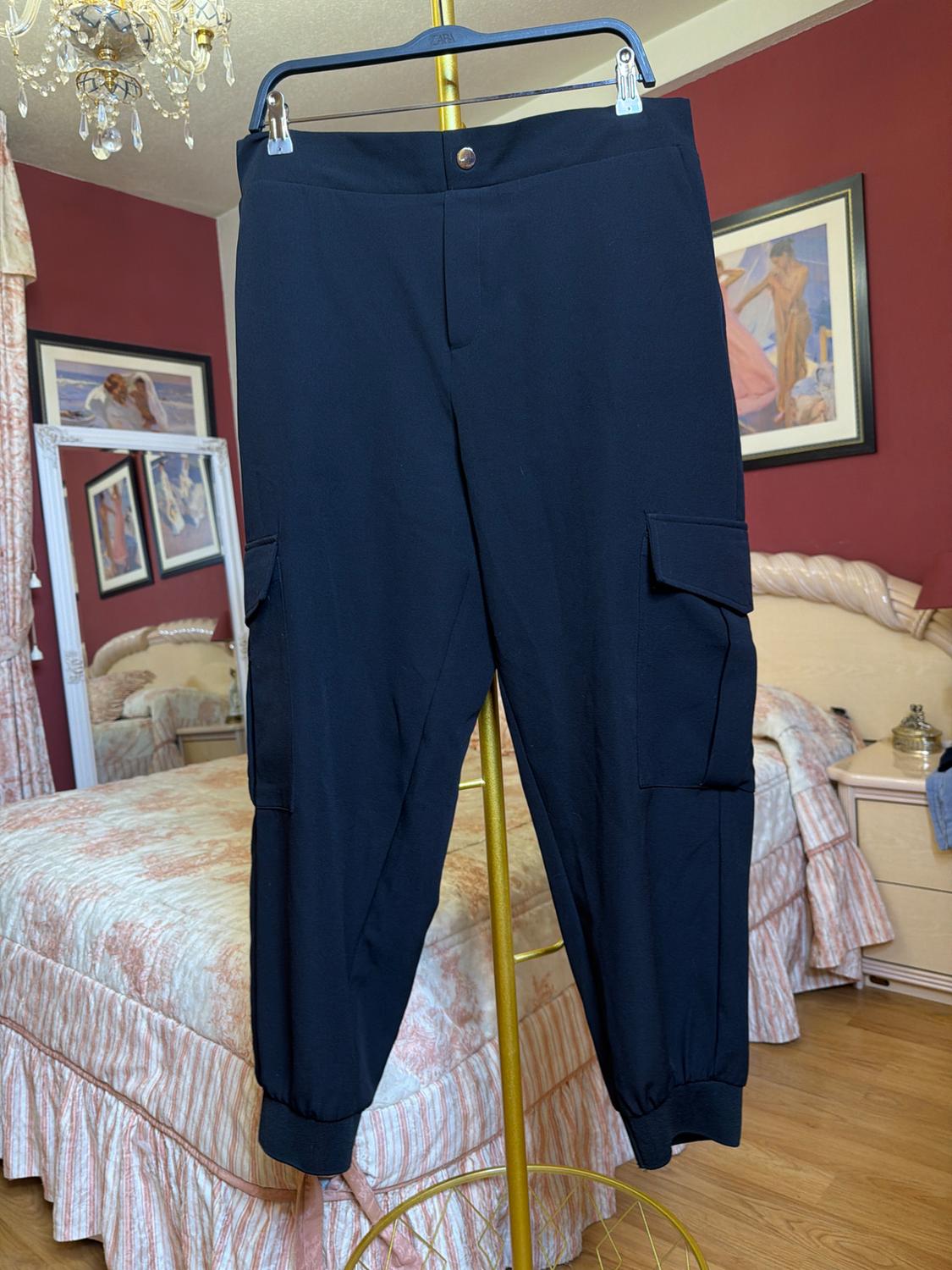 Black trousers hanging on a gold hanger in a bedroom with red walls and a bed with a patterned quilt.
