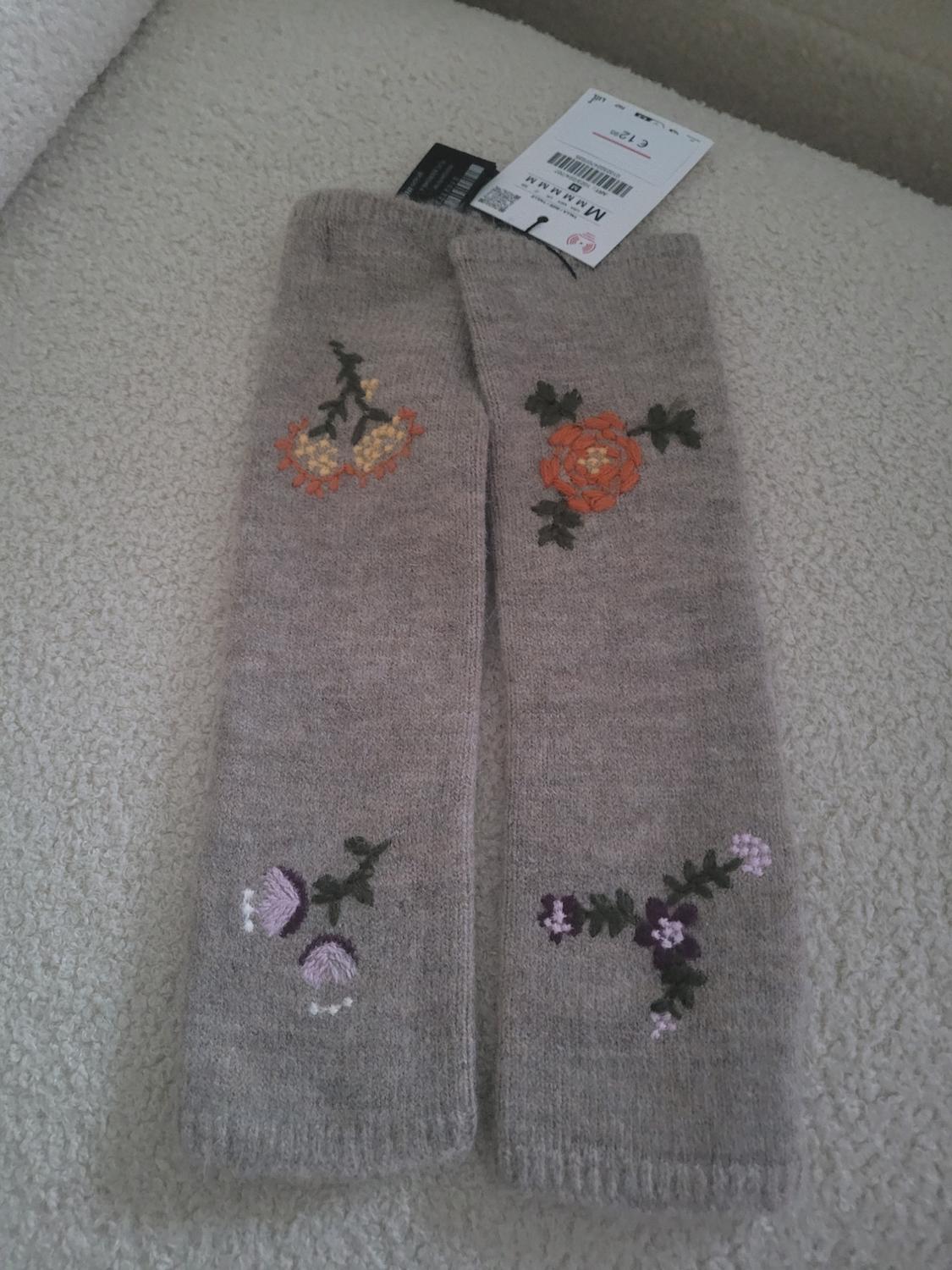 Grey socks with floral embroidery in orange and purple, on a light surface. Visible label with barcode.