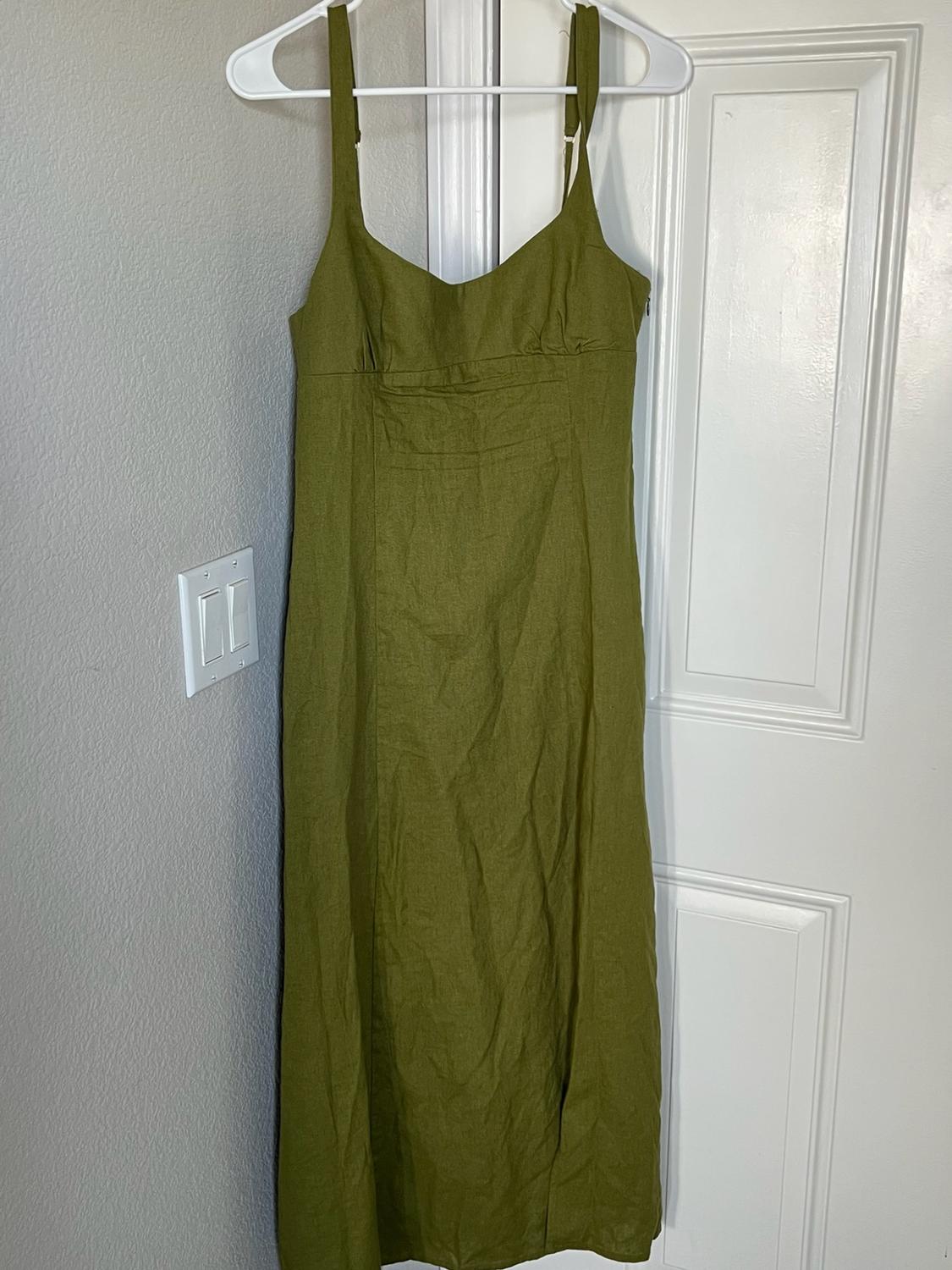 Olive green spaghetti strap maxi dress hanging on a white hanger over a white door, next to a gray wall with a light switch.