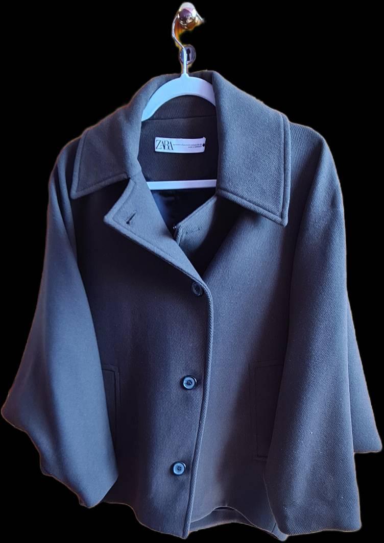 Dark grey coat with buttons and a wide collar, hanging on a white hanger. Visible label with the text "ZARA". Black background.