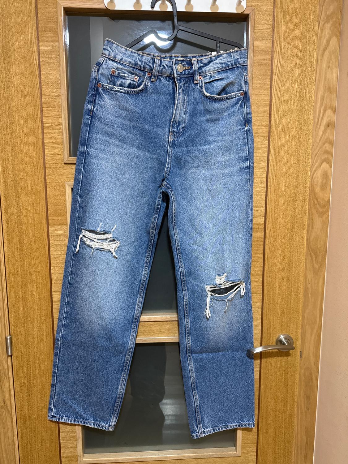 Worn blue jeans hanging on a wooden door. They have rips in both knees.