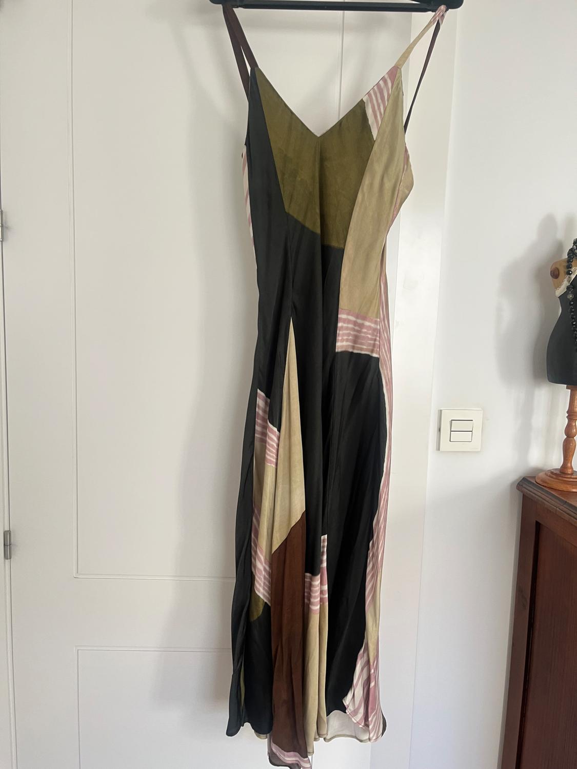 Long dress hanging on a hanger, with a patchwork design in black, green, beige and pink stripes, on a white background.