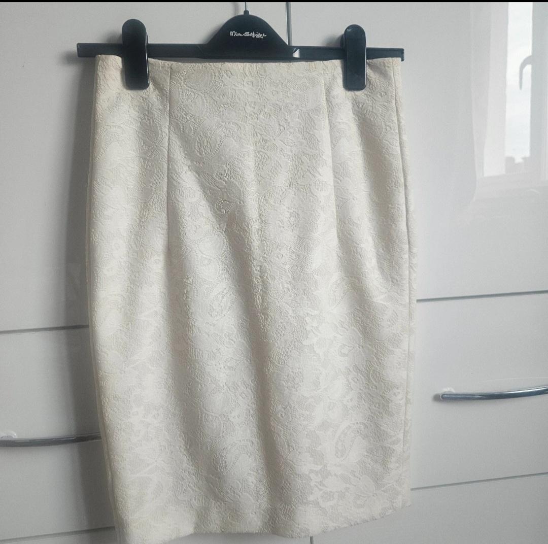 White lace skirt hanging on a black hanger against a white wardrobe background.