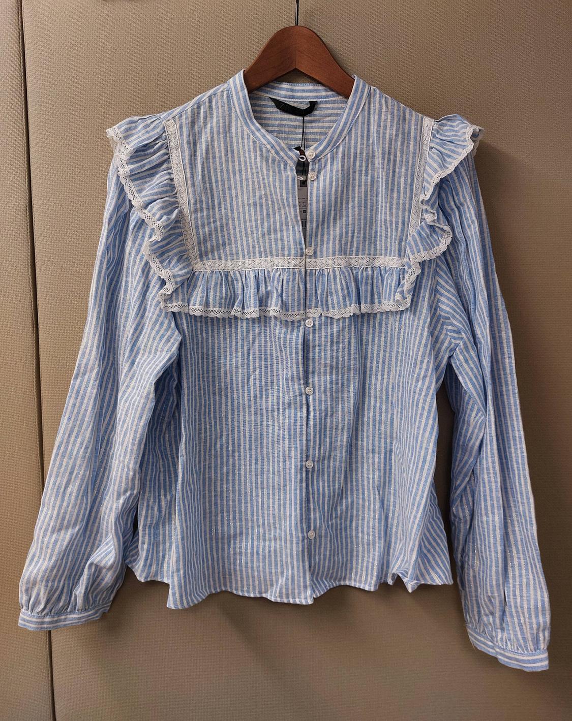 Blue and white striped long-sleeved blouse with ruffles and lace on the chest, hanging on a wooden hanger.