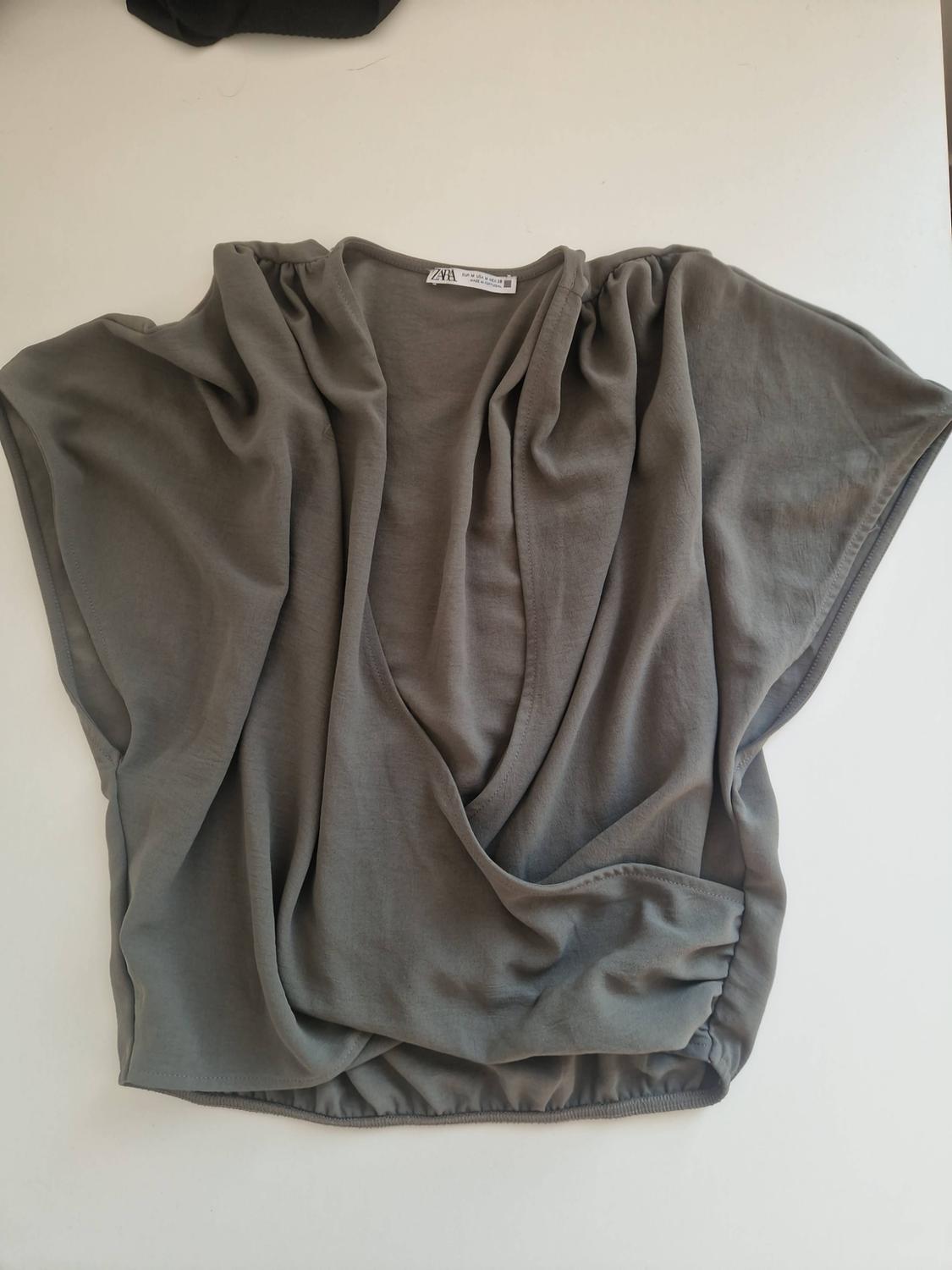 Grey short-sleeved top with a draped design, crossover neckline and elasticated hem on a white background. Label with the text ZARA.