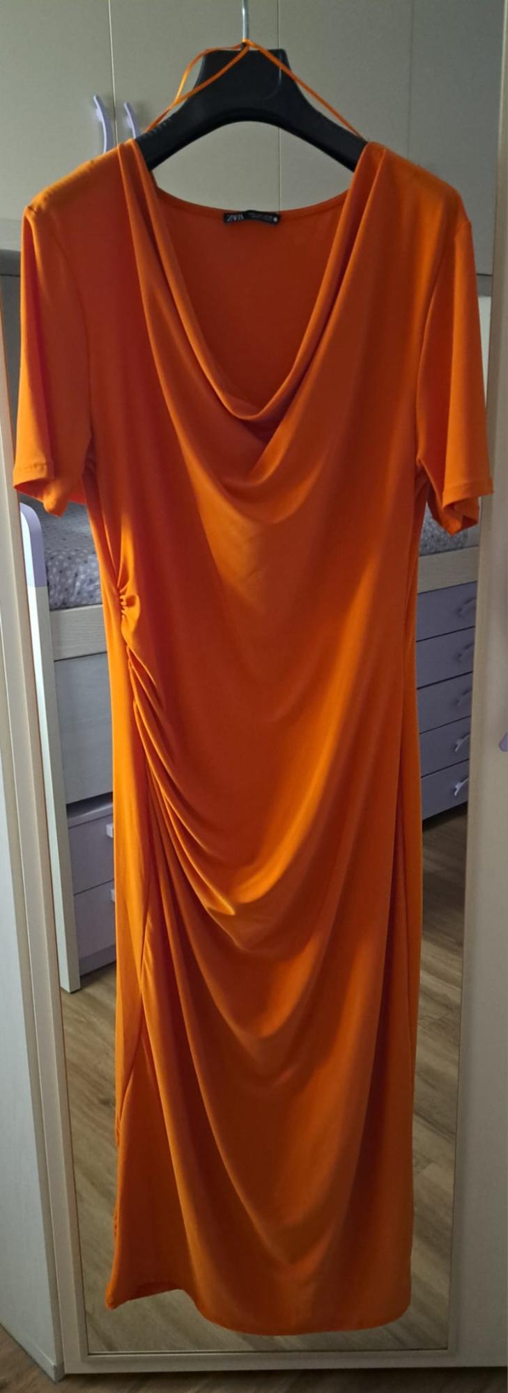 Orange short-sleeved dress with a draped neckline and side ruching. ZARA label. Hanging on a black hanger in front of a mirror.