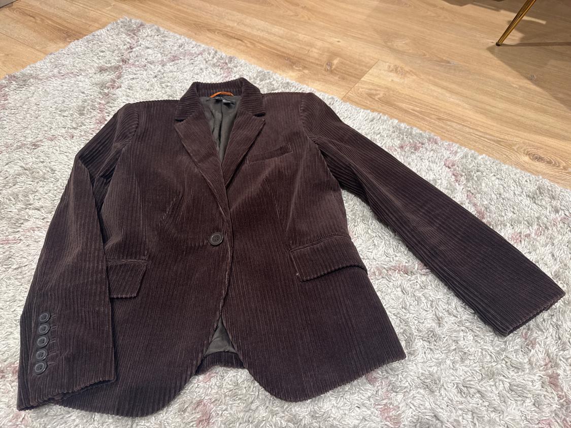 Dark brown corduroy jacket with buttons, on a grey rug and light wooden floor.