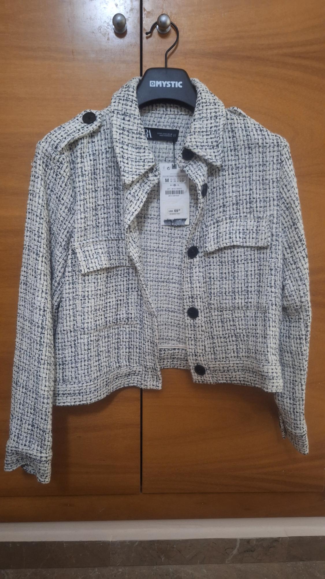 Textured jacket on a black hanger with a USD 69 price tag, hanging in front of a wooden wardrobe.