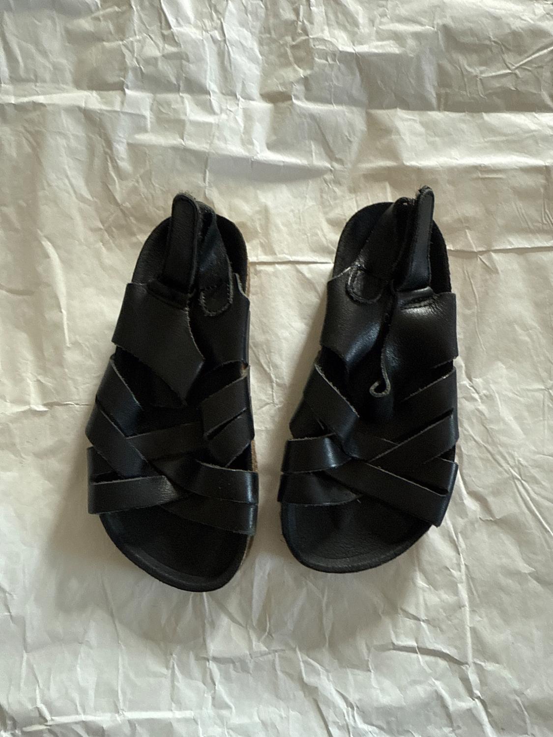 Black strappy sandals on a white crumpled paper background.