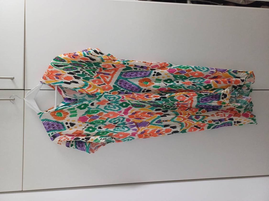 Colourful dress with an abstract print in green, orange, purple, and black tones, hanging on a white hanger against a white background.