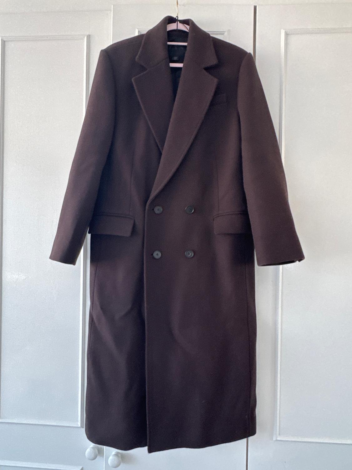 Long brown double-breasted coat hanging on a pink hanger in front of a white wardrobe.