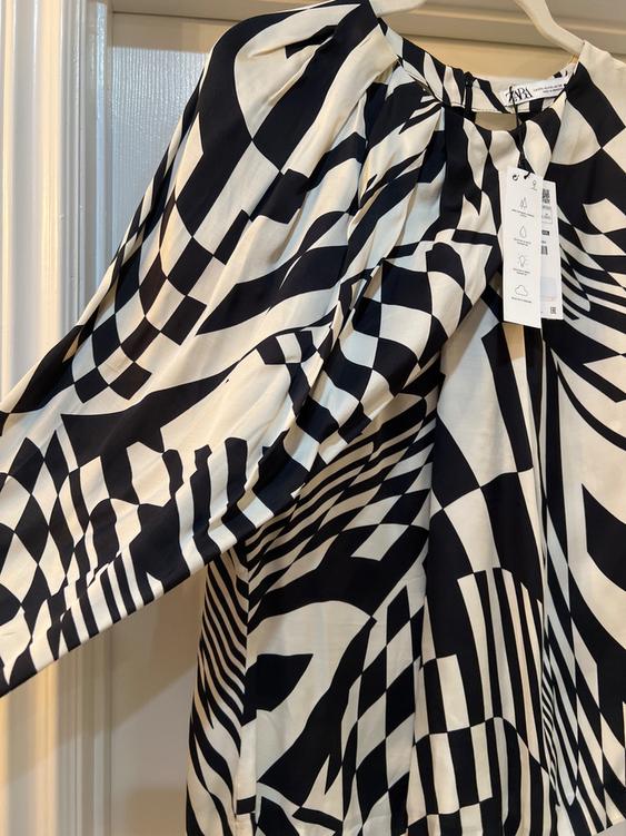 Hanging dress with black and white geometric print. Visible tag with care symbols. Indoor setting.