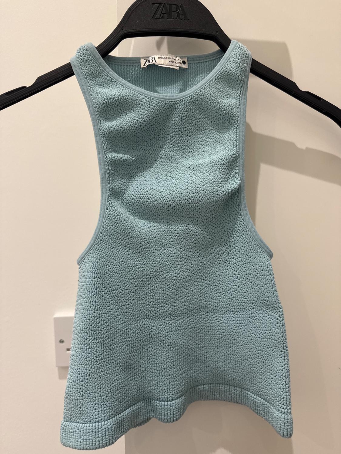 Light blue textured sleeveless top, hanging on a black hanger with the "Zara" brand visible, on a white background.