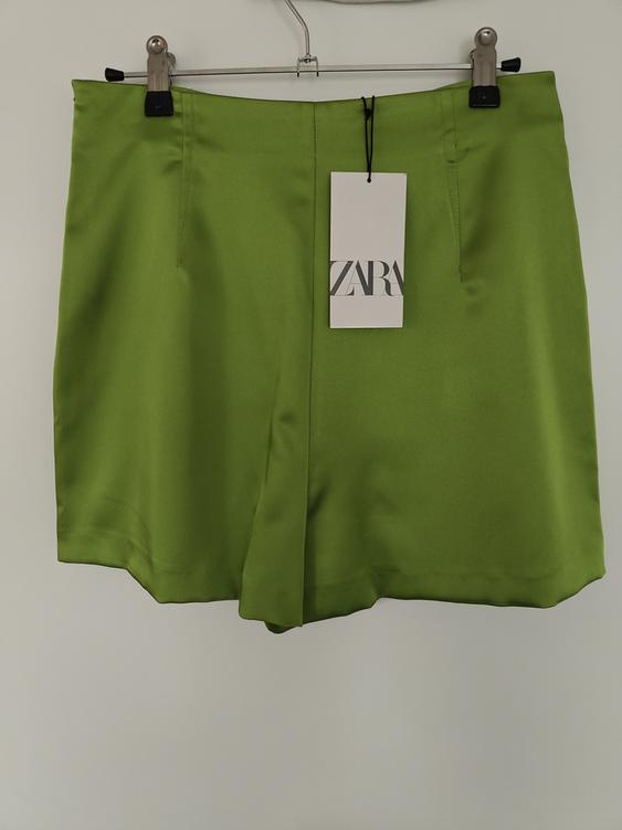 Green shorts hanging on a hanger with a label that reads "ZARA". Plain white background.