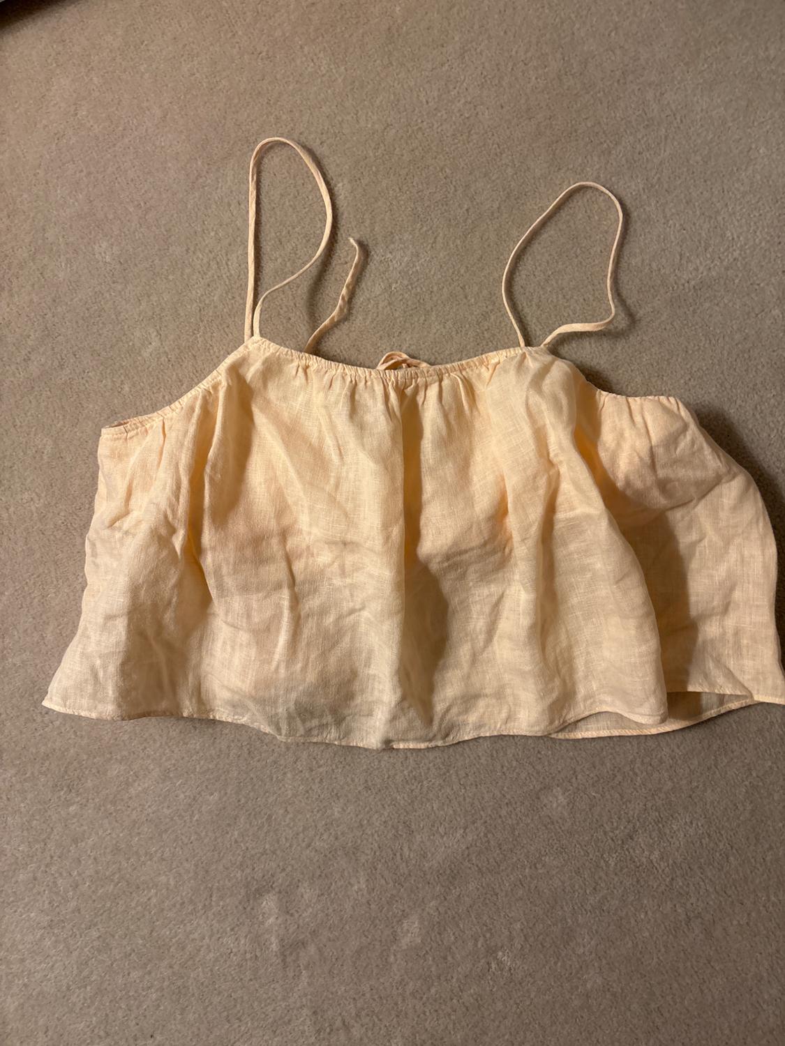 Light beige, thin-strapped crop top on a grey surface. Lightweight fabric with soft pleats.
