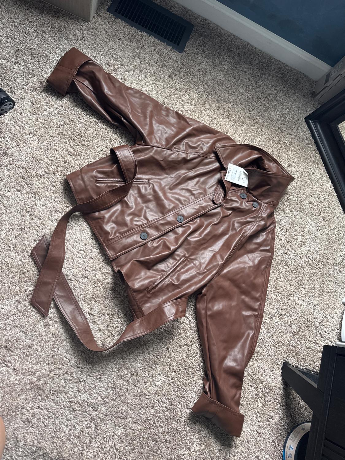 Brown jacket with buttons and a belt, viewed from above on a rug in a relaxed home setting.