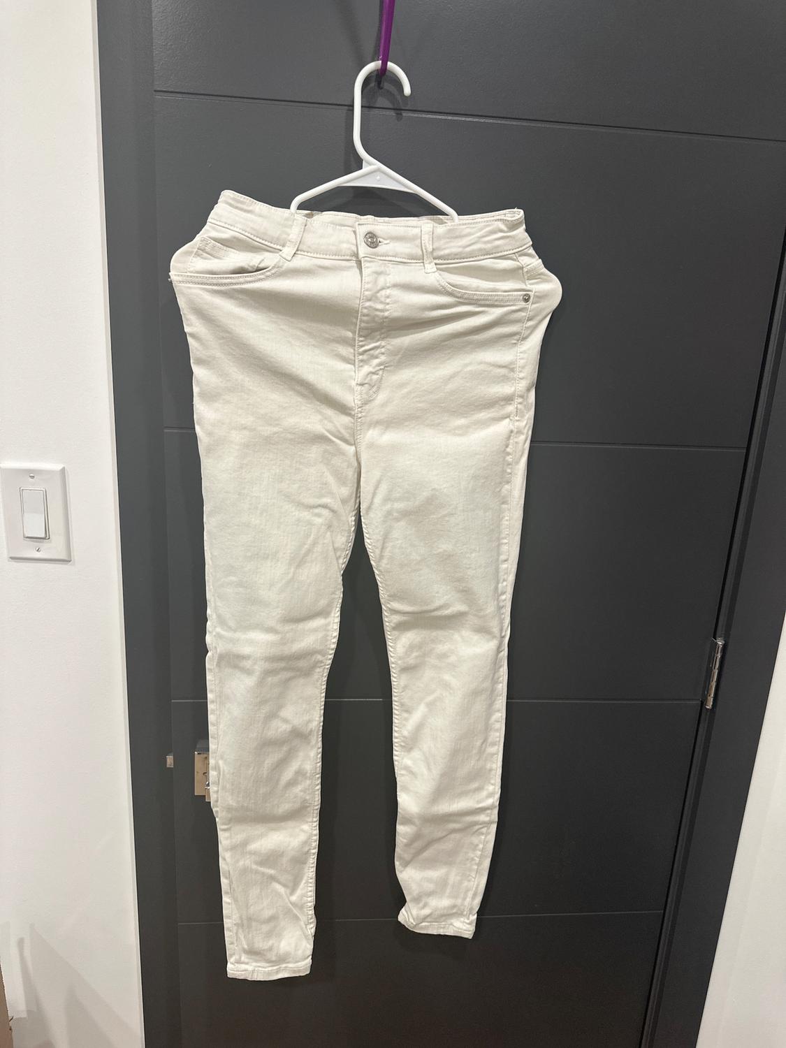 White pants hanging on a white hanger with a purple hook, over a black door. White wall background and visible outlet.