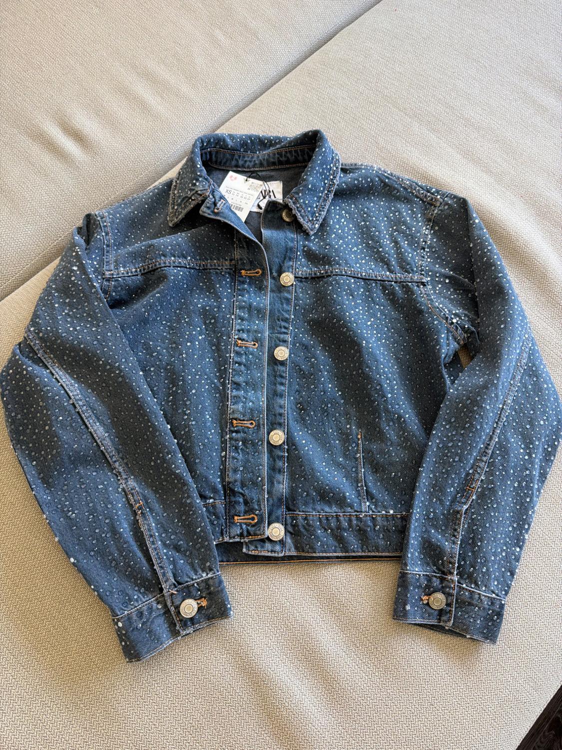 Blue denim jacket with sparkles, laid out on a fabric surface. Label with the text ZARA on the collar.