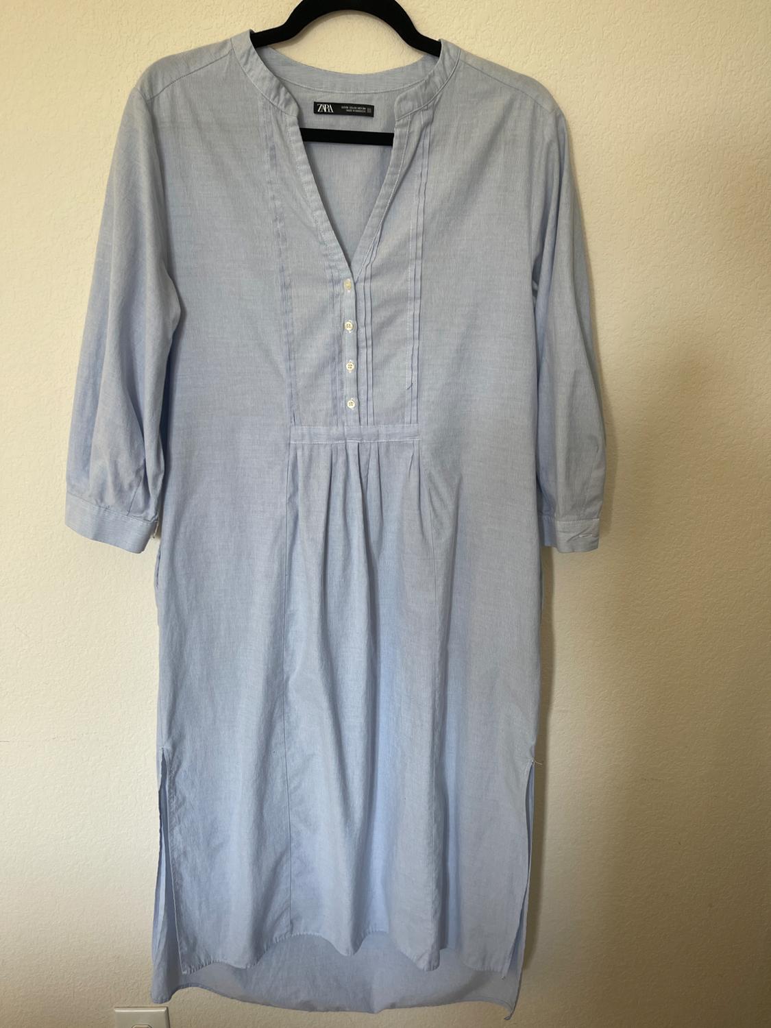 Light blue, three-quarter sleeve dress hanging on a black hanger. It has buttons on the chest and a loose, comfortable design.