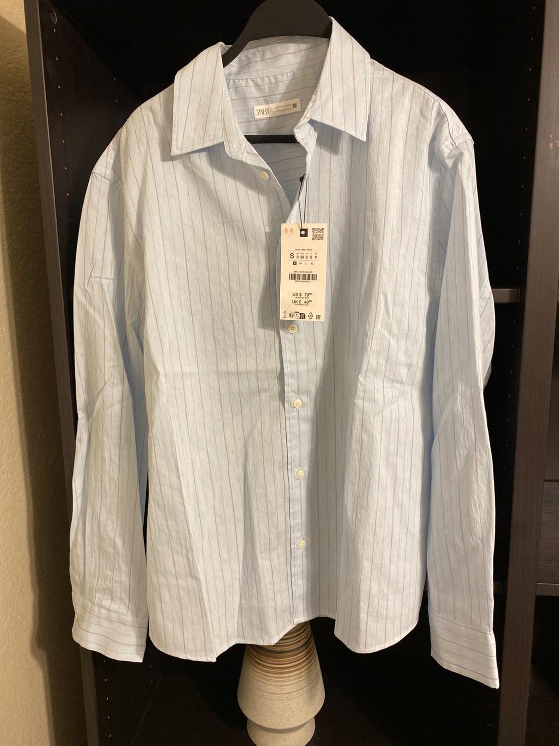 White and grey striped shirt hanging on a black hanger, with a visible label showing price and size.