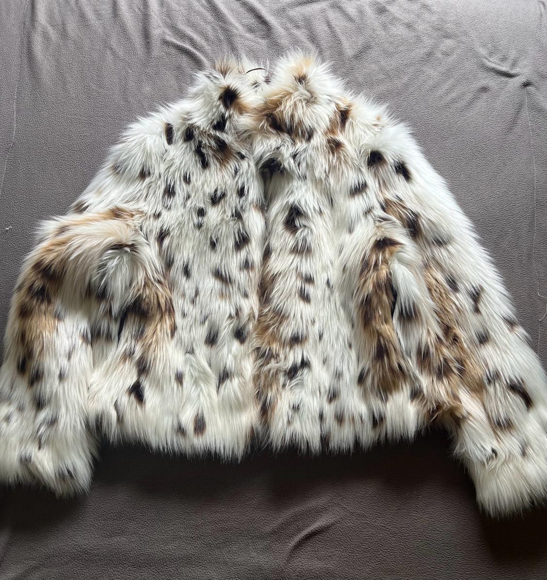 White fur coat with black and brown patches, spread out on a grey fabric background.