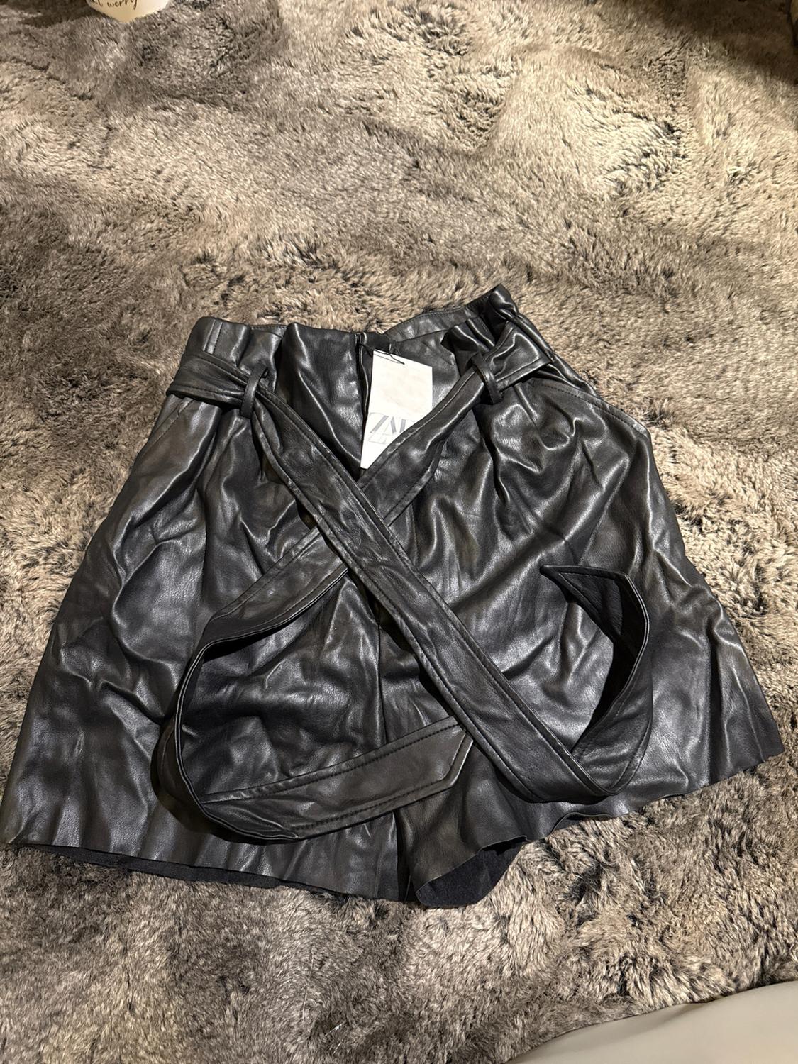 Black elastic-waist shorts with a belt and ZARA label, on a shag rug.