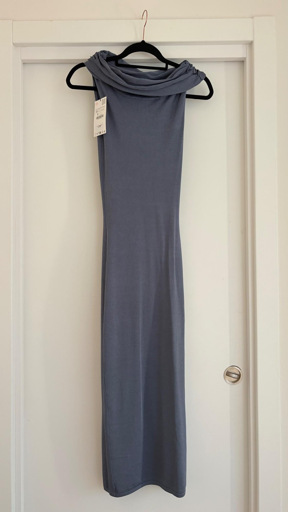Grey long dress hanging on a black hanger over a white door. Label visible on the left side of the dress.