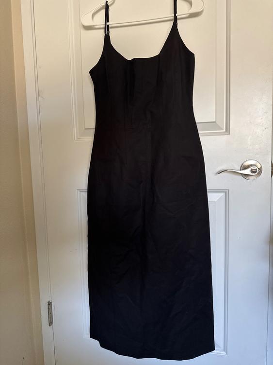 Black spaghetti strap dress hanging on a white hanger over a white door.