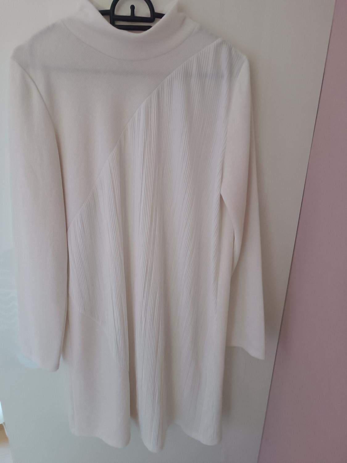 Long-sleeved white coat with a high neck and asymmetric design hanging on a black hanger against a light background.
