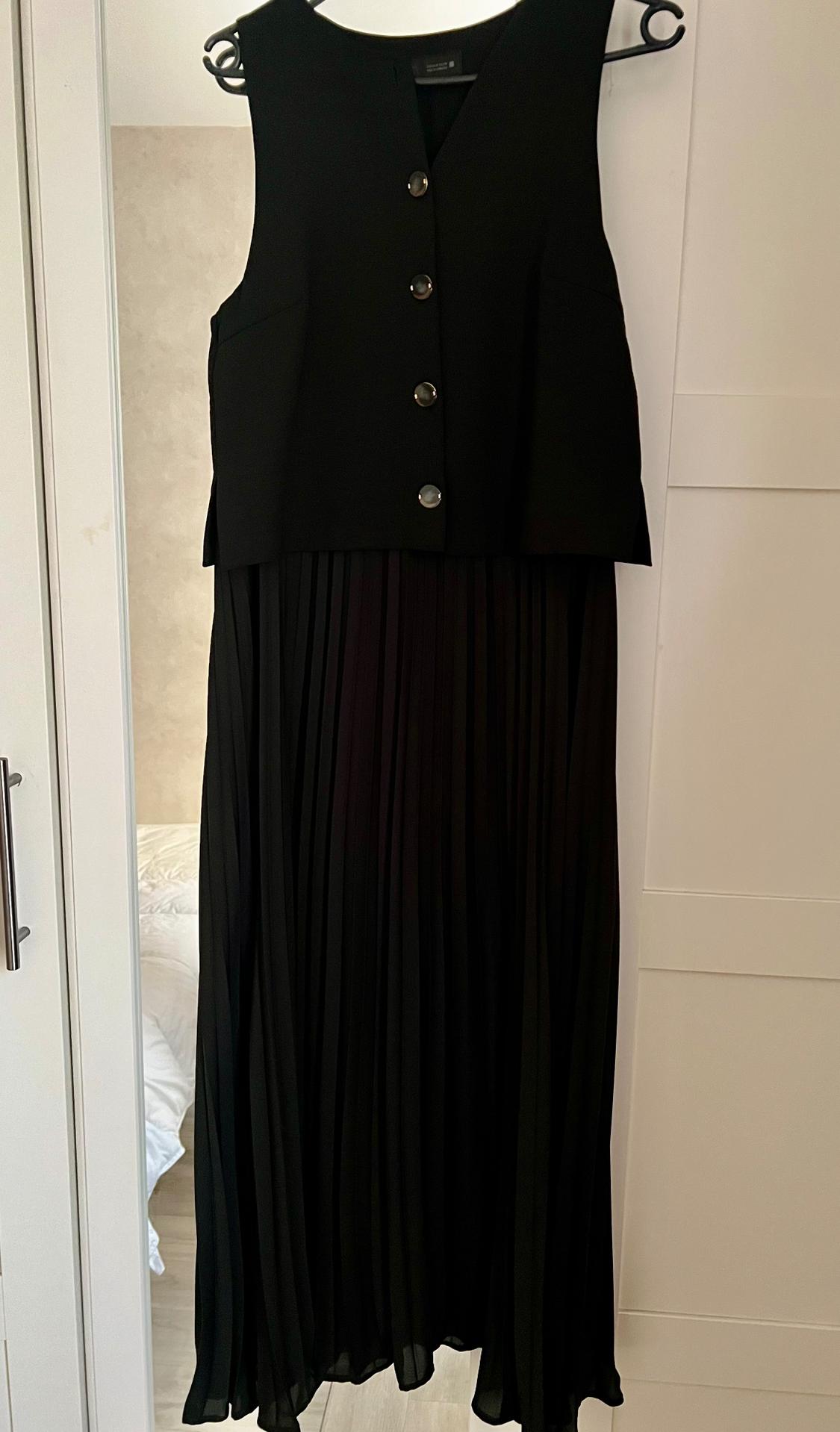 Sleeveless black dress with front buttons and a pleated skirt, hanging on a hanger inside a white wardrobe.