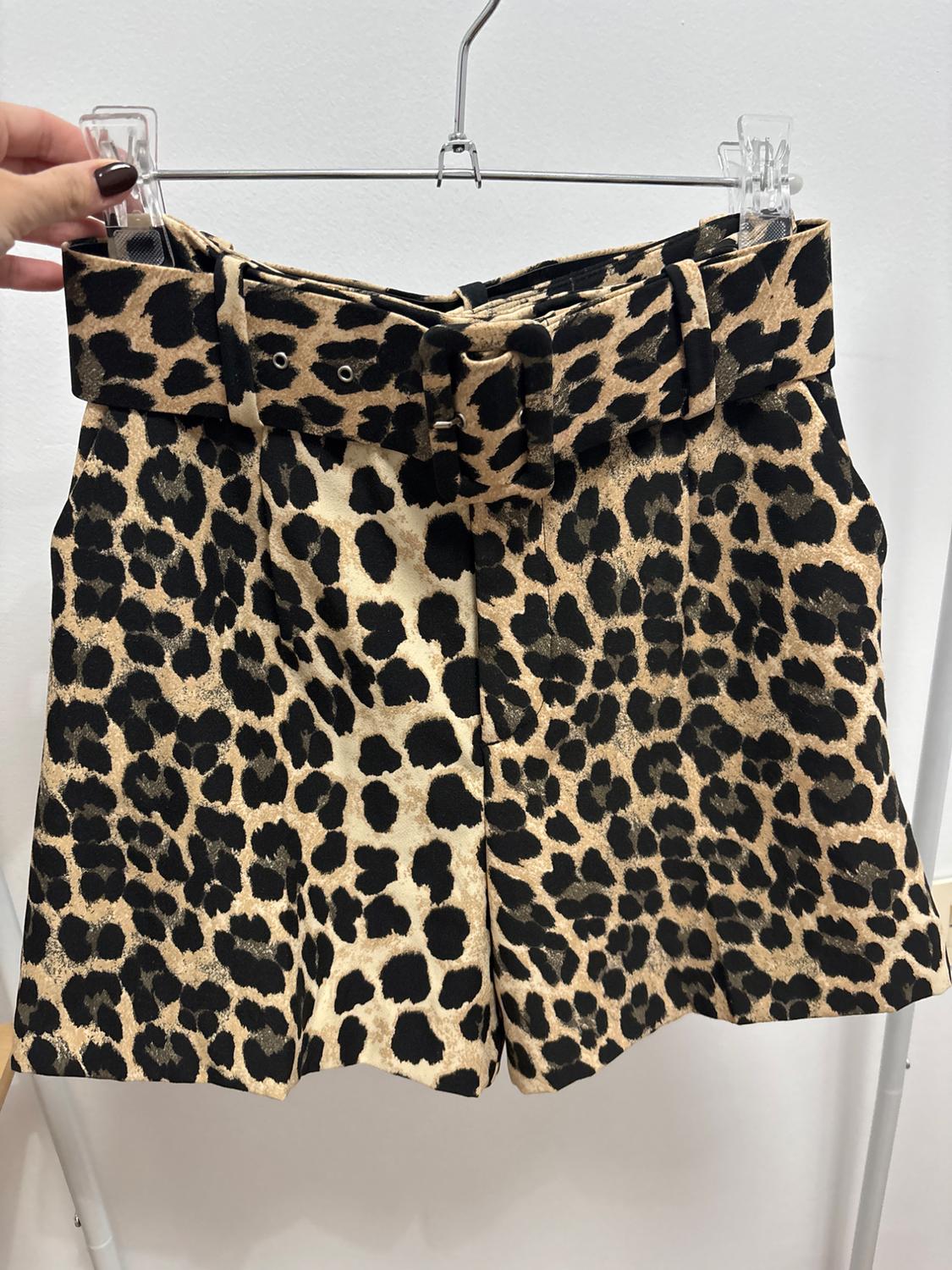 Leopard print shorts in brown and black tones, hanging on a metal hanger. Hand holding the hanger.