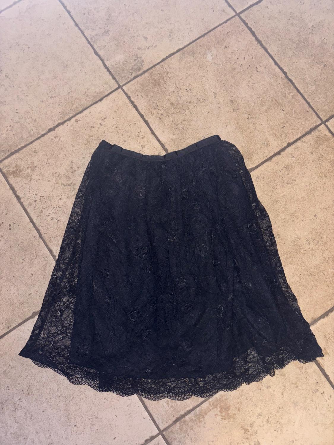 Black lace skirt with an elasticated waistband on a tiled floor. It features an inner lining and an outer layer with a scalloped hem.