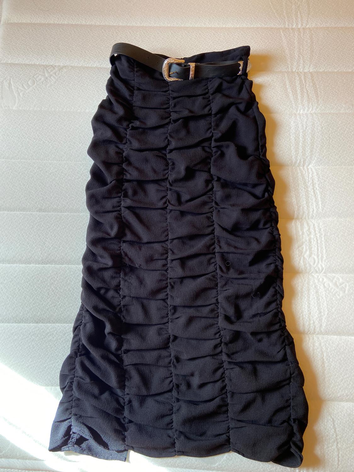 Black ruched skirt with black belt on a white padded surface.