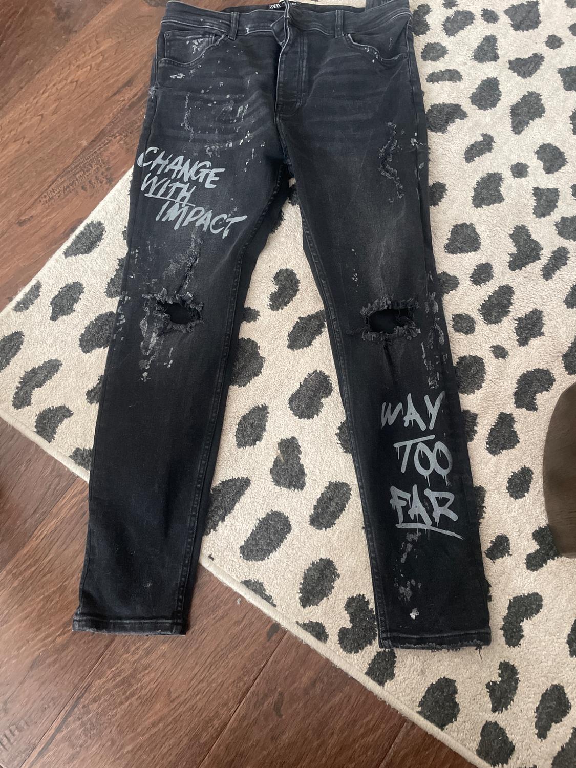 Black jeans with rips and splatter details. "CHANGE WITH IMPACT" and "WAY TOO FAR" text. On a stained carpet.