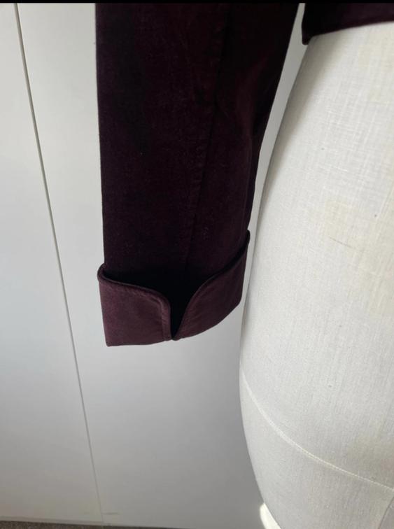 Burgundy jacket sleeve with folded cuff on a white mannequin, white wall background.