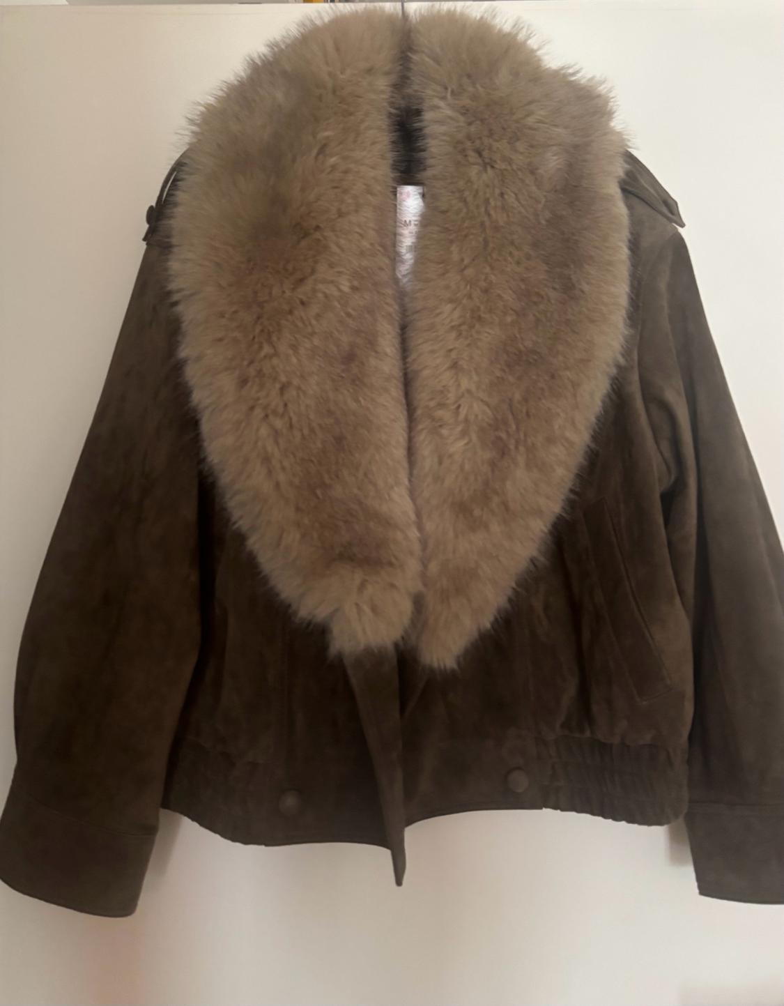 Brown faux-suede jacket with a large fur collar and an elasticated hem, hanging on a white wall.