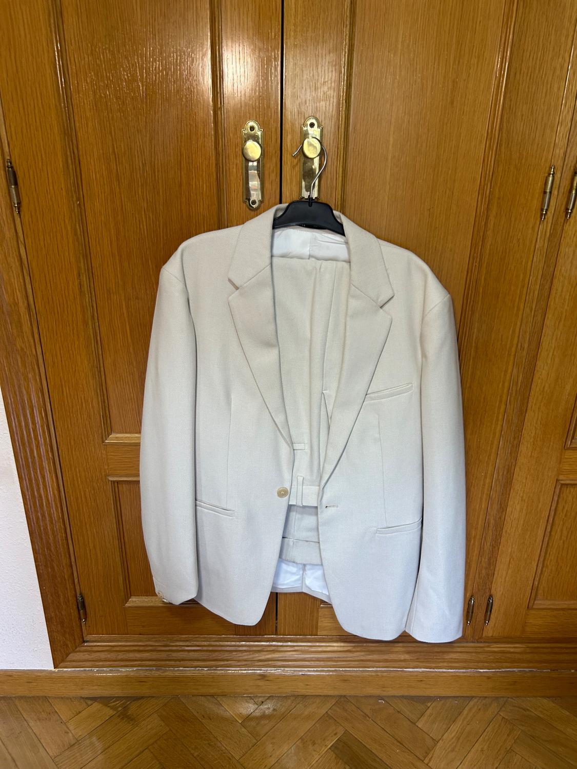 Light beige jacket and trouser suit hanging on a hanger over a classic wooden wardrobe, conveying a relaxed atmosphere.