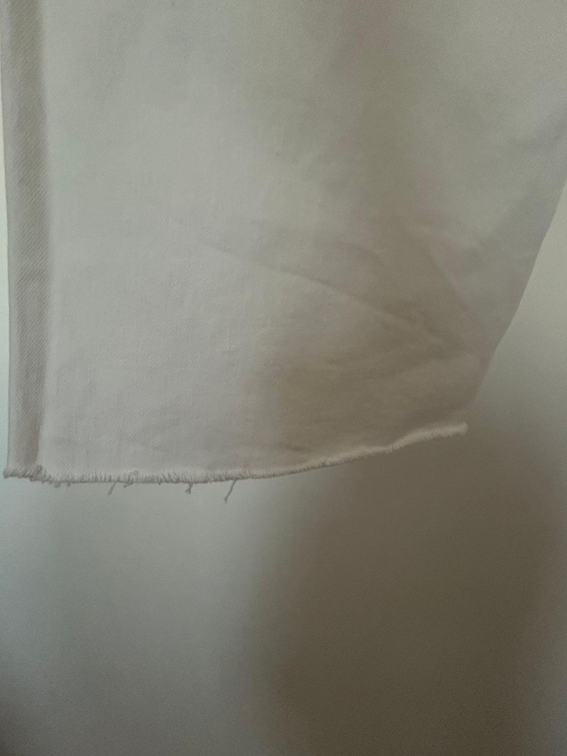 White fabric with a frayed edge, hanging against a light grey background. The texture of the weave is visible.