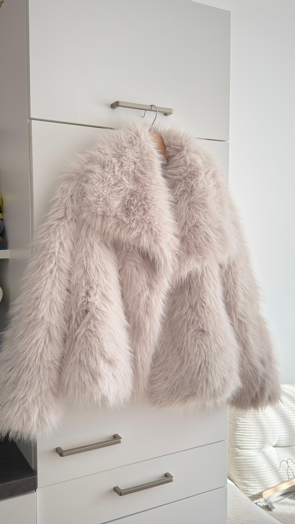 Light beige faux fur coat hanging in a white wardrobe, creating a cosy and elegant atmosphere.