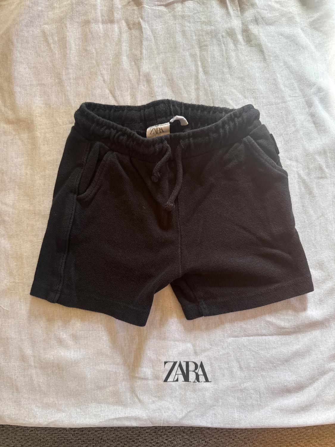 Black shorts with an elasticated drawstring waist, on white fabric with the "ZARA" logo visible at the bottom.
