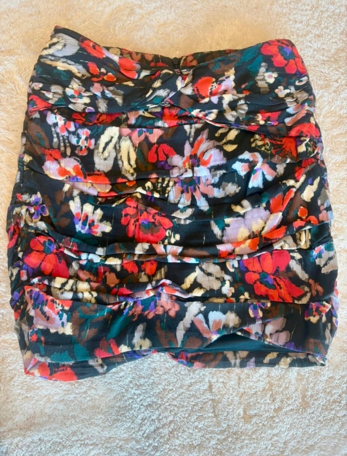 Short skirt with a floral print in red, white, and blue tones on a black background, placed on a beige surface.