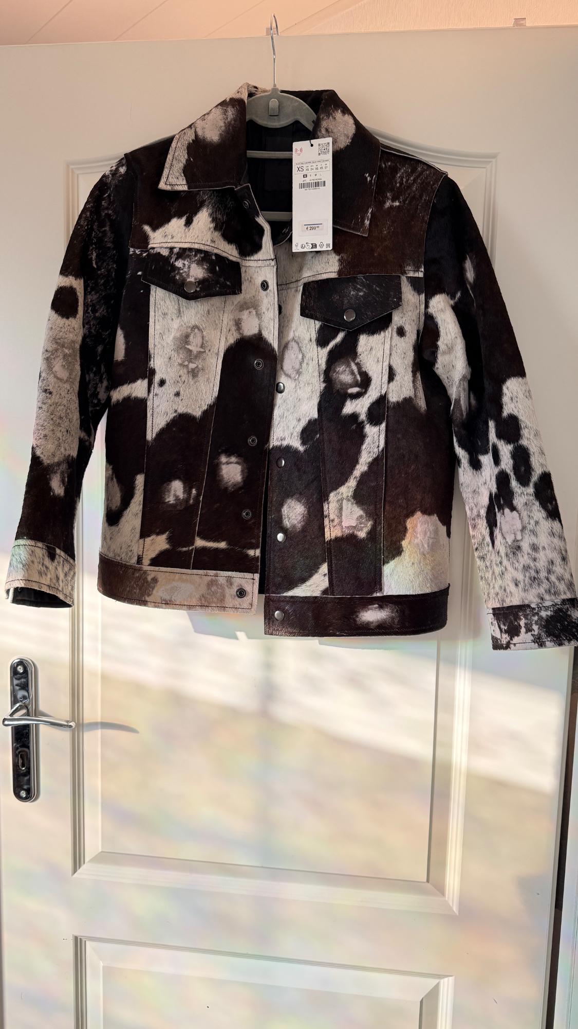 Speckled black-and-white printed jacket hung on a white door. Visible tag with product details.