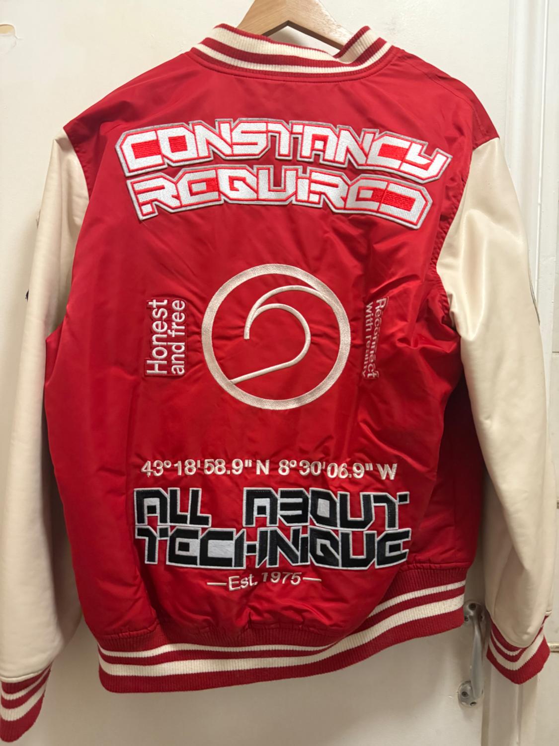 Varsity jacket in red and white with embroidered text: "CONSTANCY REQUIRED", "ALL ABOUT TECHNIQUE", coordinates and "Honest and free".