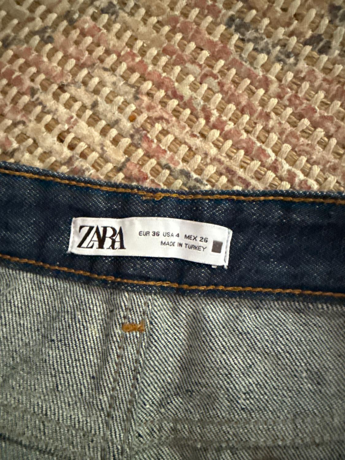 ZARA pants tag on blue denim fabric, showing sizes EUR 36, USA 4, MEX 26, made in Turkey. Braided fabric background.