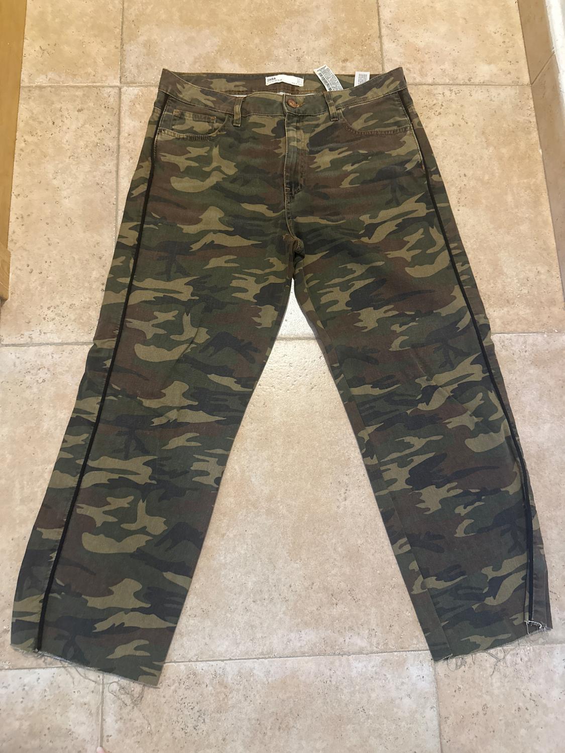 Green and brown camouflage trousers on a beige tiled floor. Tags visible on the waistband.