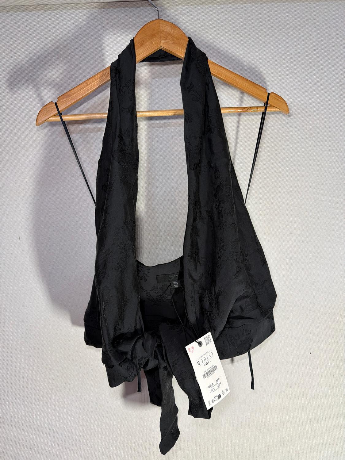 Black top hanging on a wooden hanger, with a visible tag showing size S and a barcode, against a white background.